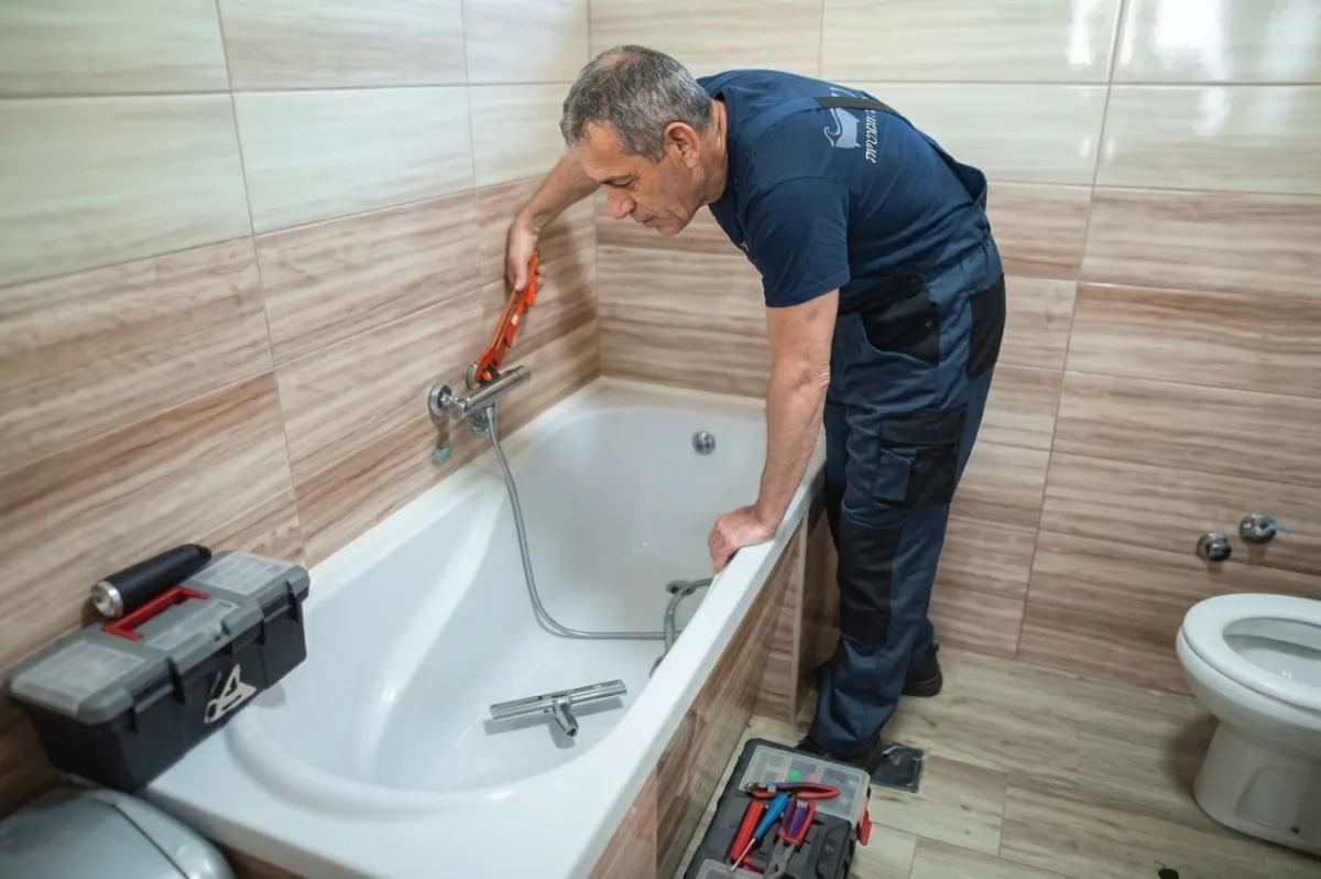 טכנאי גל אמבטיות מחליף ברז אמבטיה בעזרת מפתח צינורות