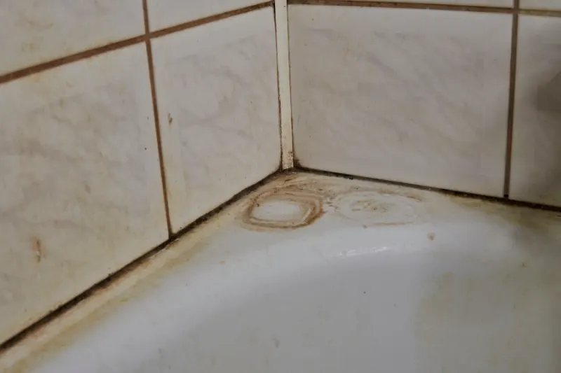 פינת אמבטיה עם אריחים מוכתמים וחלודה — לפני